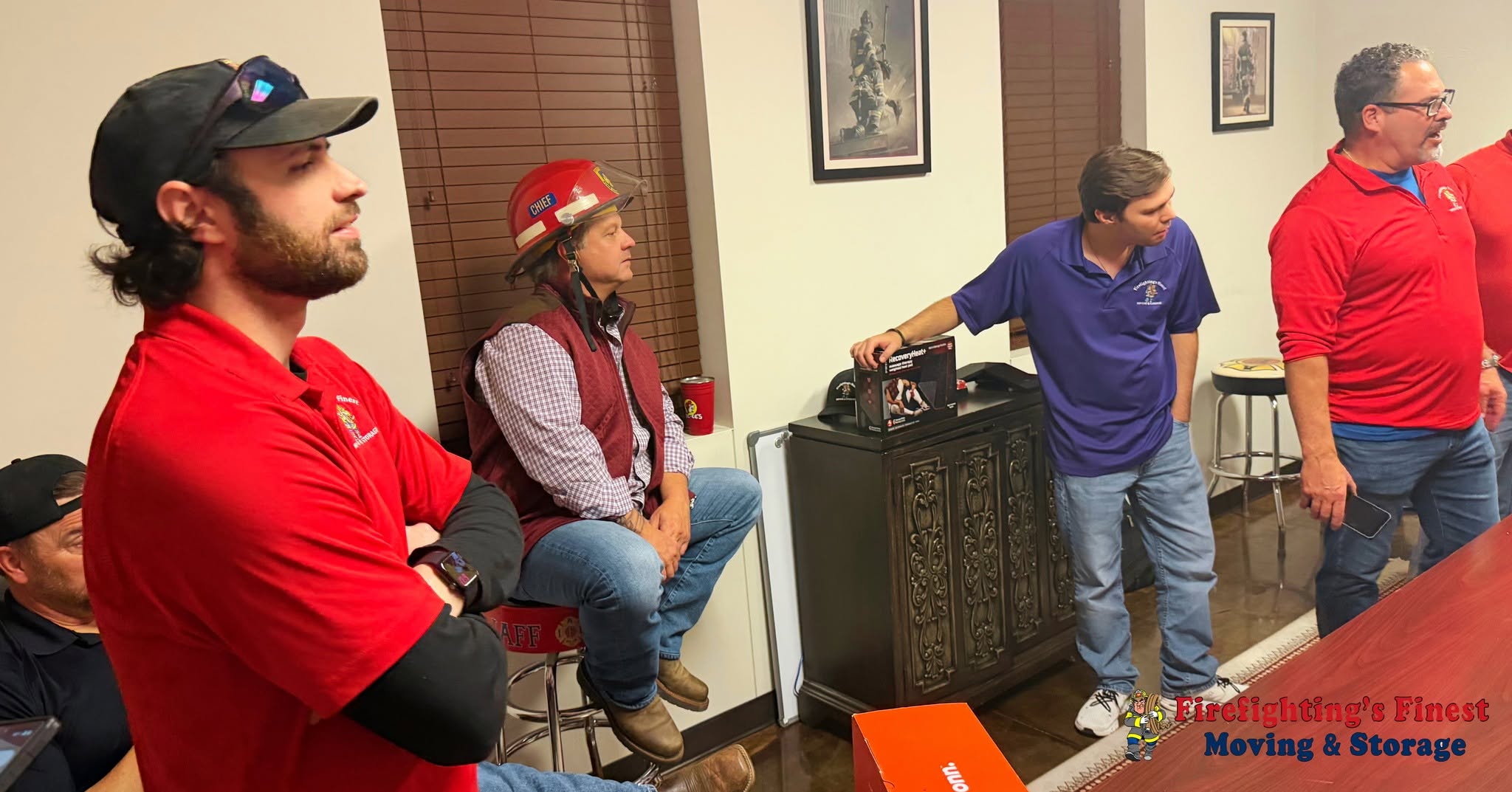 Staff members from Firefighting's Finest Moving & Storage gathered for a team meeting, including one wearing a red fire chief helmet, representing our dedicated local moving professionals serving Carrollton, TX.