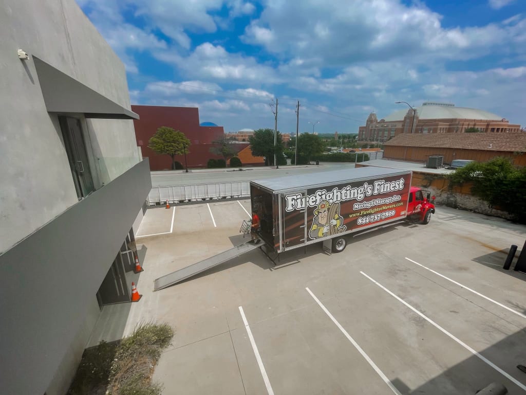 Firefighting’s Finest Moving & Storage branded moving truck being unloaded in a spacious parking lot in Texas